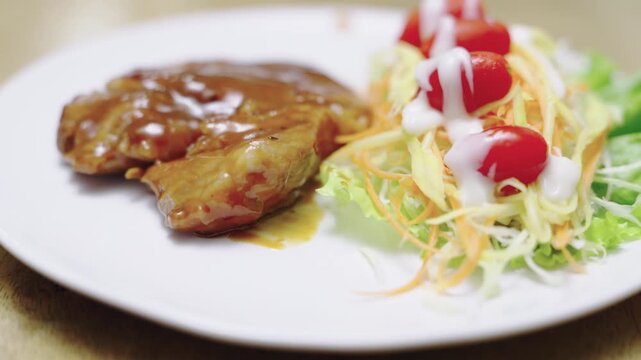 Juicy grilled meat steak glazed with savory brown gravy served on a white plate with fresh shredded vegetable salad and cherry tomatoes. Healthy protein dinner meal with creamy white dressing.
