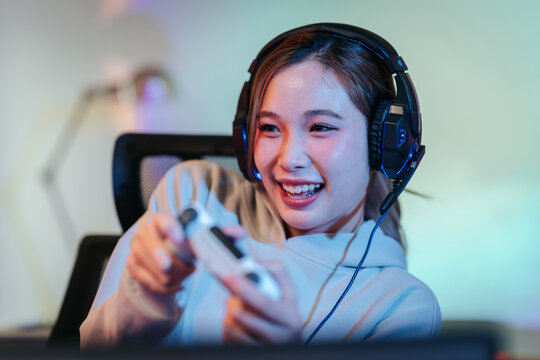 A cheerful female gamer wears gaming headphones enjoying a thril