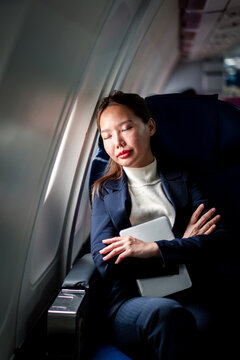 Tired businesswoman sleeps on airplane during flight holding tab