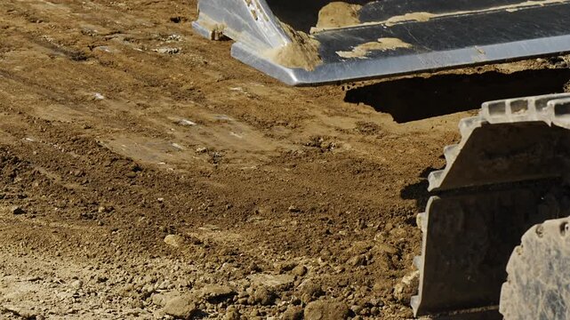Heavy machinery digger bucket moving and leveling sand and gravel at an active industrial construction site representing earthmoving operations