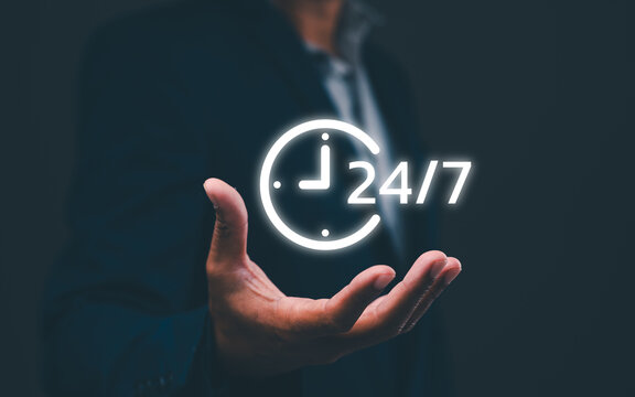 A person in a suit holds a glowing 24/7 clock icon, symbolizing continuous or round-the-clock service or availability.
