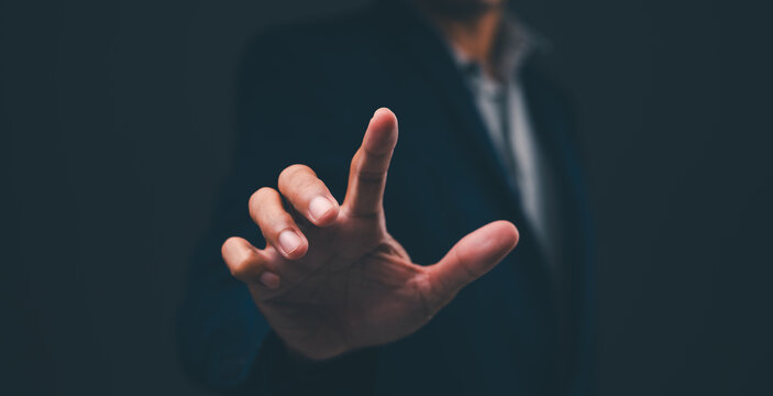 A person in a dark suit reaches forward with an outstretched hand against a dark background, suggesting interaction or a touch gesture.