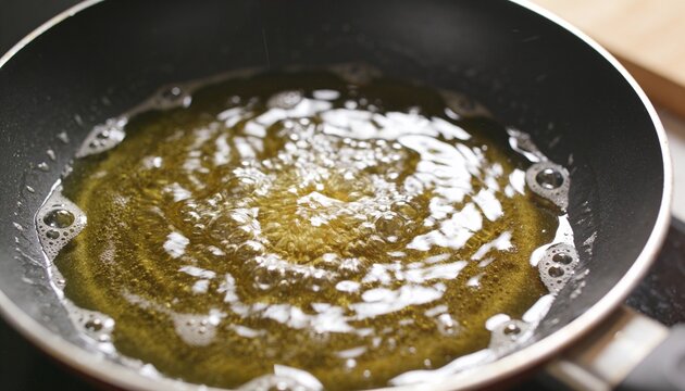 Sizzling non-stick frying pan heating hot oil on stove, bubbling foam with handle and wood counter