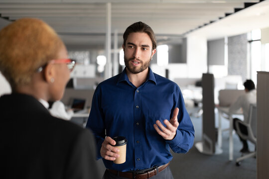 Young man speaking with black female colleague in office