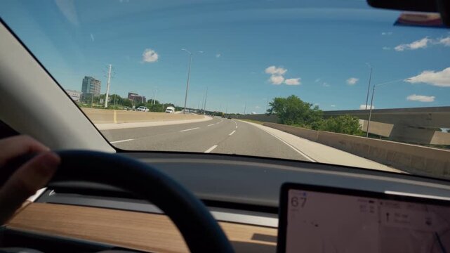 POV point of view inside an electric vehicle cruising on a multi-lane highway during a sunny summer day. Interior dashboard with steering wheel
