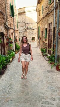 happy woman smiling face tourist walking through beauty old town. adul girl explores enjoys ancient architecture cobbled stone streets, historical village houses decorated with flower pots plants.