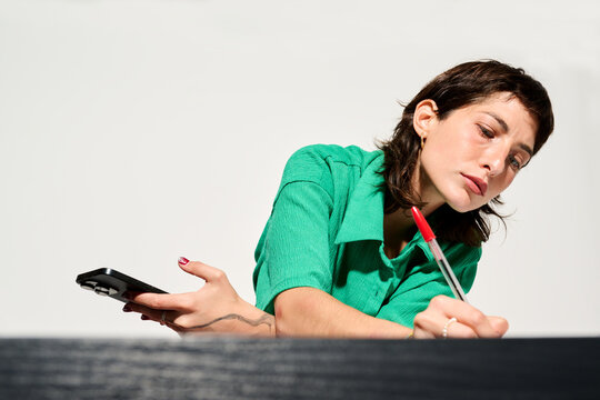 Woman writing with pen holding mobile phone