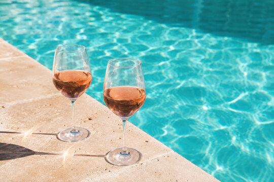 Glasses of tasty rose wine on swimming pool edge, space for text