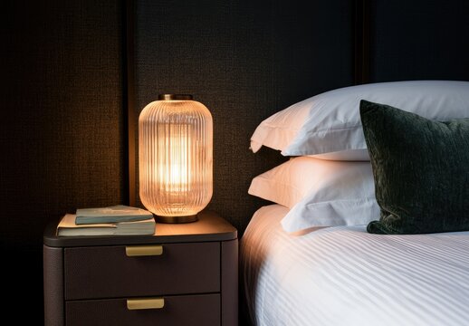 Modern bedside table with glowing lamp and luxurious bedding
