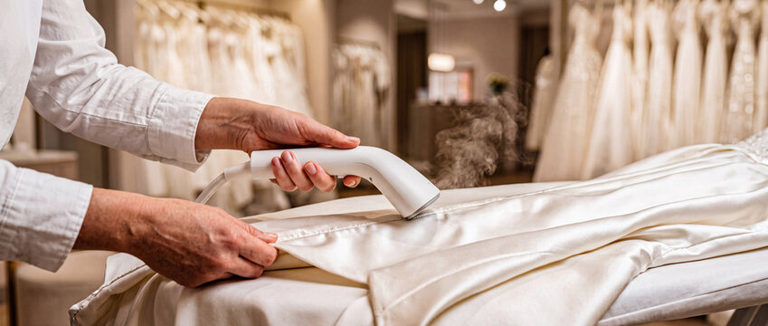 Bridal dress steaming in boutique wedding shop preparing satin gown for fitting and alterations