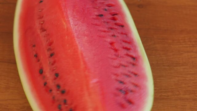 A slice of ripe red watermelon rotating on a textured wooden table surface with a static camera view. High speed fps footage for summer food commercial, organic fruit and refreshing dessert video. 