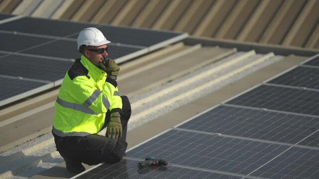 The kneeling inspector points along the panel rows, directing final checks across the array as the day winds down on the rooftop site, filmed as part of a commercial clean energy