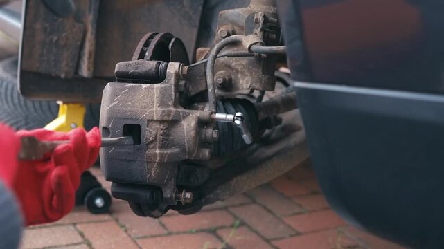 Compressing brake pads and caliper piston during brake service with brake fluid release process. Automotive repair concept with disc brake maintenance, exposed caliper components and manual adjustment