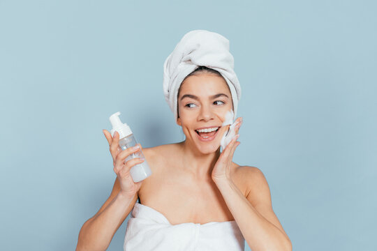 Happy woman wraps towel around head while applying face wash