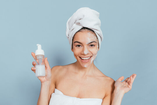 Cheerful woman with face mask, holding bottle against blue background