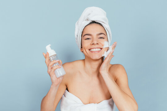 Happy woman in white towel applies skincare product