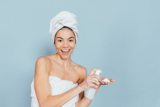 Smiling woman in towel holds spray bottle against light blue background