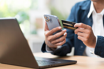 Fototapeta premium Shopping online concept. Close up of hands holding credit card during shoping online on mobile phone with laptop computer on table