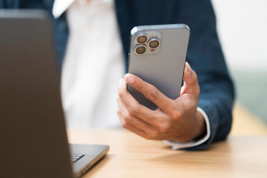 Hands of business man holding mobile phone during using laptop computer on table
