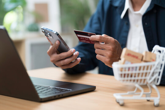 Shopping online concept. Close up of hands holding credit card during shoping online on mobile phone with laptop computer on table
