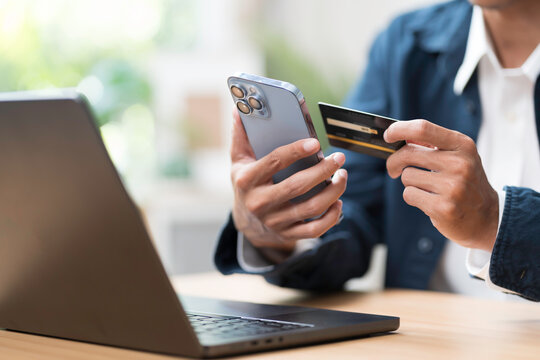 Shopping online concept. Close up of hands holding credit card during shoping online on mobile phone with laptop computer on table