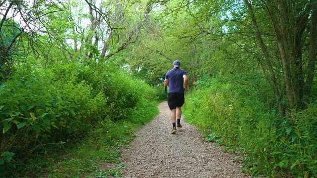 Beginner runner exercising on forest trail with determined steady pace. Middle aged man improving fitness while overcoming overweight challenges. Cardio workout, healthy habits, endurance training