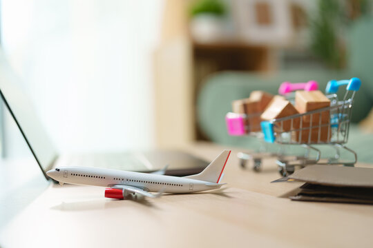 Model airplane with shopping carts, parcel boxes, laptop and wallet cross-border e-commerce, online shopping, global shipping, logistics, digital payment and international delivery