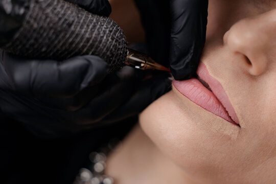 Female adult receiving lip tattoo: closeup of permanent makeup application