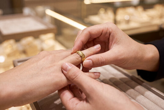 Close up of a person trying a classic gold ring on their finger over a display case while shopping for fine jewelry in a store