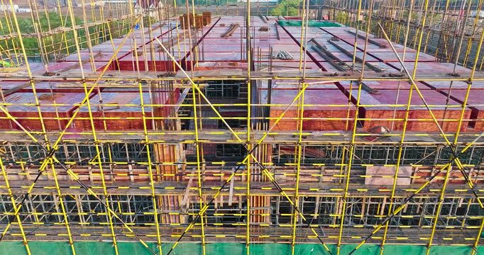 High angle view of a modern building construction site framed by intricate yellow scaffolding and wooden formwork.