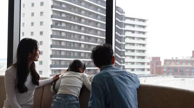 ホテルラウンジの窓際で景色を眺める30代日本人夫婦と6歳の子どもの後ろ姿