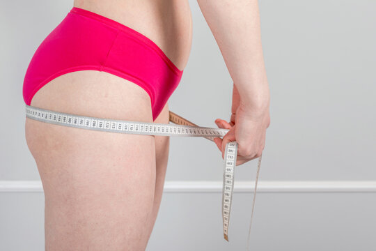Pregnant woman measuring hip circumference with tape. First trimester maternity health check and body monitoring. Concept of physical change and weight management during early pregnancy
