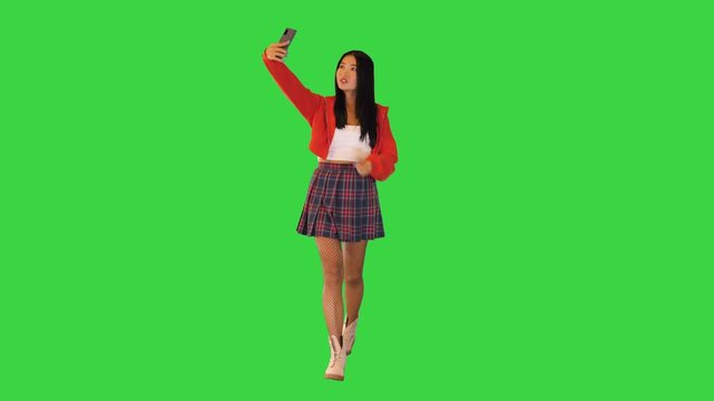 Lighthearted asian girl takes a selfie while walking on a Green Screen, Chroma Key.