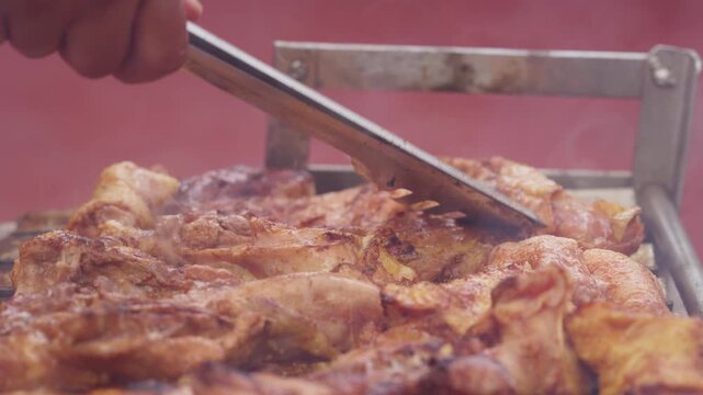 Close Up of Chef Hand Turning Seasoned Barbecue Chicken with Tongs on Grill with Smoke