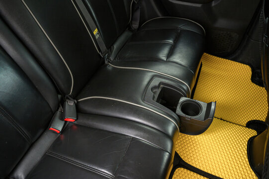 black leather seats with white stitching, a built‑in cup holder, and bright yellow textured floor mats with black trim