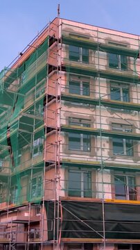 Modern residential building under construction covered with green protective safety netting on a warm summer evening. Construction site with unfinished facade. Urban development 