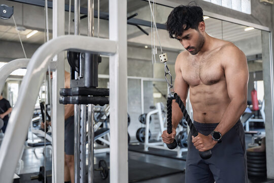 Focused muscular Asian man performing triceps pushdown exercises on a cable machine during an intense strength training workout inside a modern fitness center building healthy endurance.