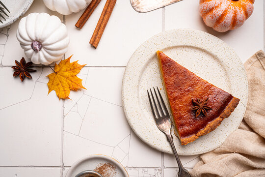 Piece of american pumpkin pie with cinnamon on white tile background, top view
