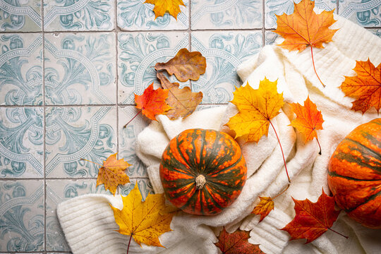 Cozy autumn flat lay with pumpkins, knitted woolen sweater and autumn leaves candle on tile background. Autumn home decor. Cozy fall mood. Thanksgiving. Halloween.