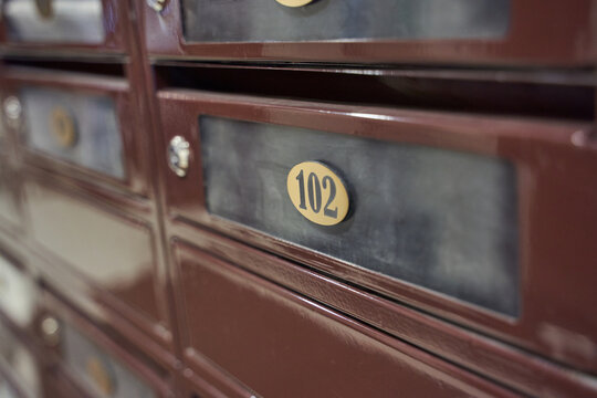 Row Of Metal Mailboxes With Closeup Compartment Labeled 102 Showing Brass Number Plate And Worn Textured Surface In Interior Postal Corridor.
