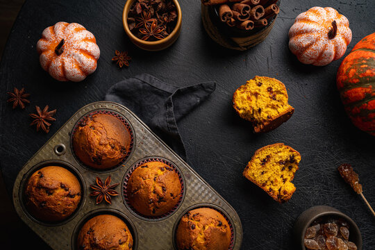 Homemade autumn pumpkin muffins with cinnamon and chocolate on dark background, top view