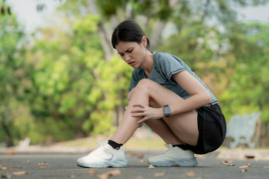 Young woman suffering calf pain while squatting after running in park, holding sore leg muscle, sports injury and muscle cramp outdoor fitness concept. calf, pain, cramp, leg, running, runner, injury,