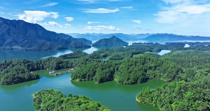 Aerial view of green forested islands scattered across a tranquil blue lake with mountains under a bright sunny sky in Hangzhou, China.