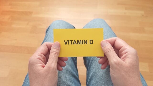 First-person point of view of a woman sitting in jeans and holding a bright yellow card with the text Vitamin D written on it.