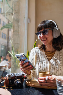 A girl with a phone in her hands enjoys the moment. Portrait of a smiling young woman sitting in a cafeteria with a mobile phone in her hands.