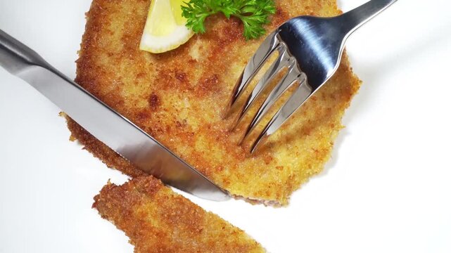 Wiener Schnitzel schneiden mit Gabel und Messer auf wei&szlig;em Hintergrund 