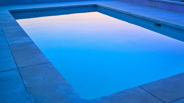 Showing swimming pool reflecting sunset light shifting from pink to blue at pool deck, with skimmer