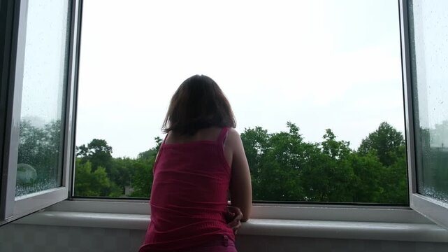 Girl looks out of window during rainy day in residential area