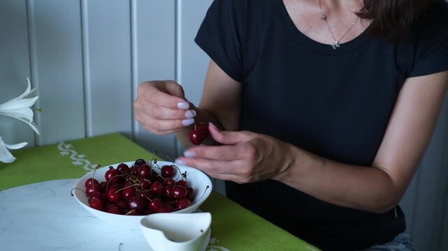 A woman is eating ripe, delicious sweet cherries in her kitchen at home.