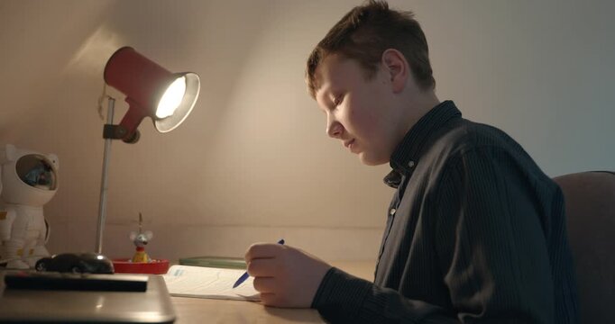Kid Boy Doing Homework in Workbook Writing with Pen on Table Desk. 4K 10-bit